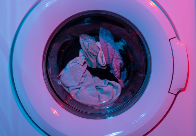 Colorful washing machine with clothes inside, lit by vivid purple and blue lights.